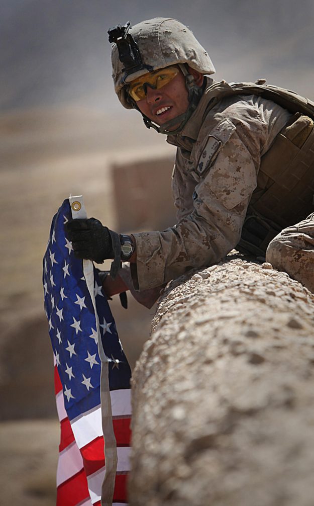 U.S. Marine Corps Cpl. Jorge Villarreal, a motor transportation mechanic with India Battery, 3rd Battalion, 12th Marine Regiment, Regimental Combat Team 2, displays a U.S. flag atop the wall of a compound Sept. 29, 2010, in Kajaki district, Helmand provin